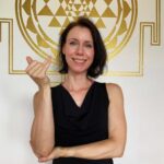Die Yoga- und Meditationslehrerin Stefanie Seher demonstriert mit der rechten Hand Vishnu Mudra für die Wechselatmung und stützt zugleich mit der linken Hand den rechten Ellenbogen.